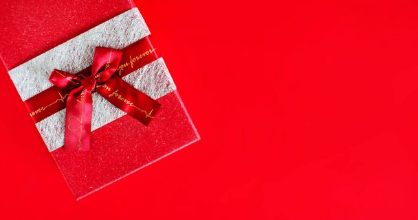 rode geschenkdoos met strikje op een rode achtergrond. kopieerruimte - Foto, afbeelding