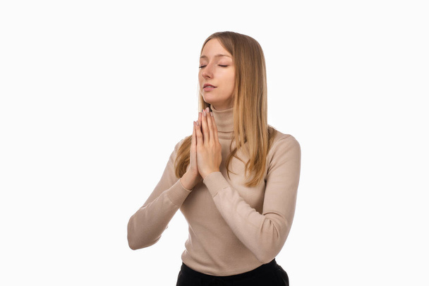 Attractive blond girl in casual clothes prays for wellness of family, keeps palms pressed together in praying gesture, saying namaste. Human emotions, gesture concept. Studio shot white background - Fotografie, Obrázek