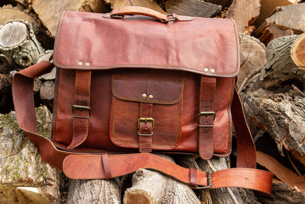 Vintage handmade leather briefcase bag sitting on wood pile outdoors ready for adventure journey - Photo, Image
