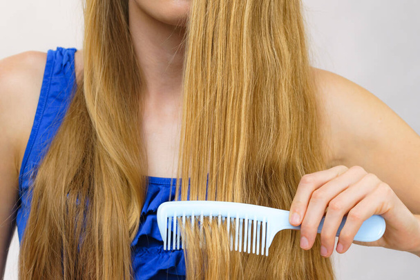 Young woman combing long healthy blonde hair, using comb - Fotoğraf, Görsel