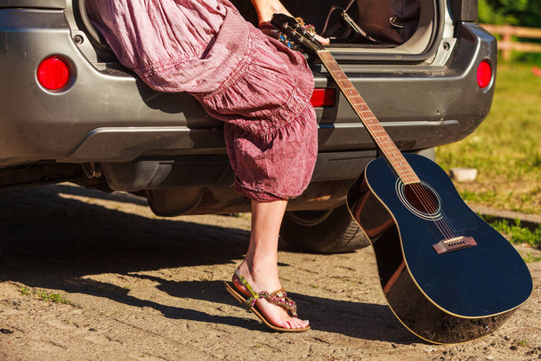 Seyahat gezisi otostop konsepti. Yaz kızı hippi stili akustik gitarlı hatchback arabada oturuyor. - Fotoğraf, Görsel