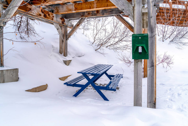 Яркий синий стол для пикника со скамейками под деревянным павильоном на снежном холме - Фото, изображение