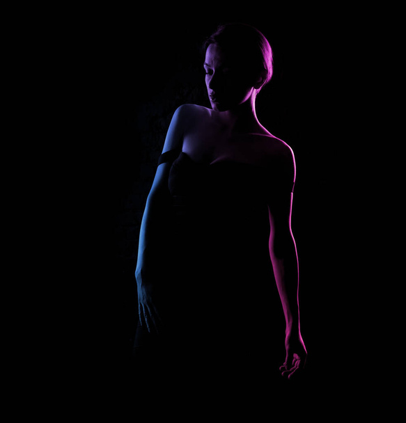 Silhouette of a beautiful woman body on a dark background. Blue and pink light. - Фото, изображение