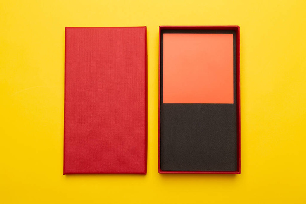 Red box product packaging with blank orange card isolated on yellow background. Flat lay. - Valokuva, kuva