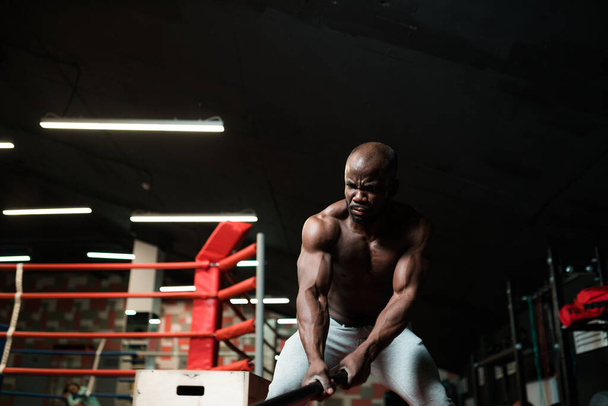A male African American in white pants in the gym leaned forward to do the exercise - Foto, Imagem