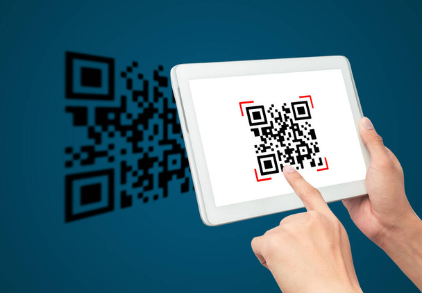 Mit der Hand scannt der Tablet-Computer den QR-Code auf blauem Hintergrund. Bargeldlose Technologie und Digitalgeld-Konzept. - Foto, Bild