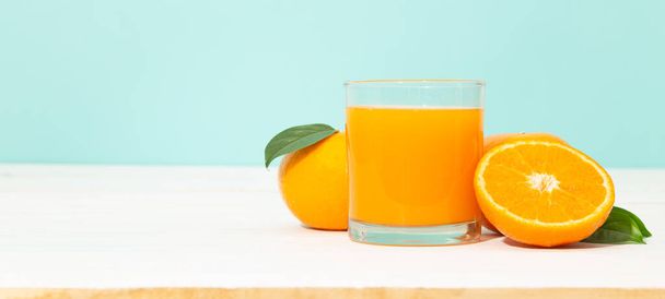 Świeży sok pomarańczowy w szkle i pomarańcze owoce na białym drewnianym stole z niebieskim tle baner z miejsca kopiowania. - Zdjęcie, obraz