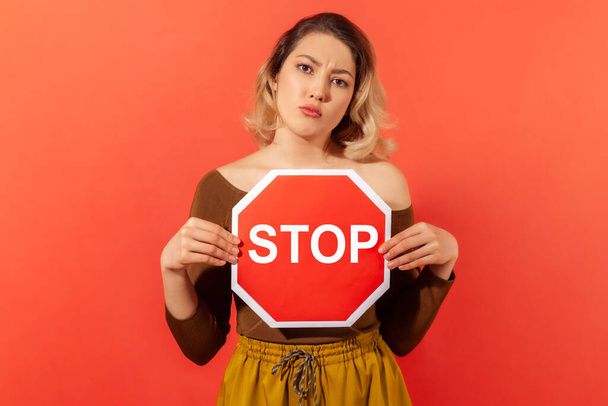 Serious woman holding and showing red stop sign, concerned about women rights, demanding equality. Indoor studio shot isolated on orange background - Foto, Bild