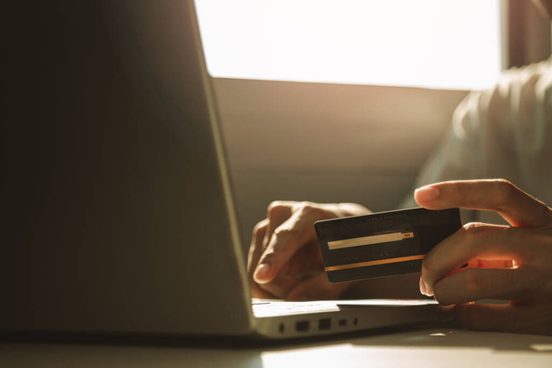 クレジットカードを持っている男性の手と自宅で仕事から休憩しながら、オンラインショッピングのための作業机でラップトップコンピュータを使用して、電子商取引、インターネット銀行. - 写真・画像