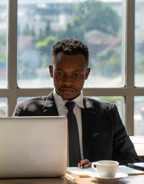Porträt eines jungen afrikanischen Geschäftsmannes, der schwarzen Anzug trägt und im Büro arbeitet. Geschäftskonzept - Foto, Bild