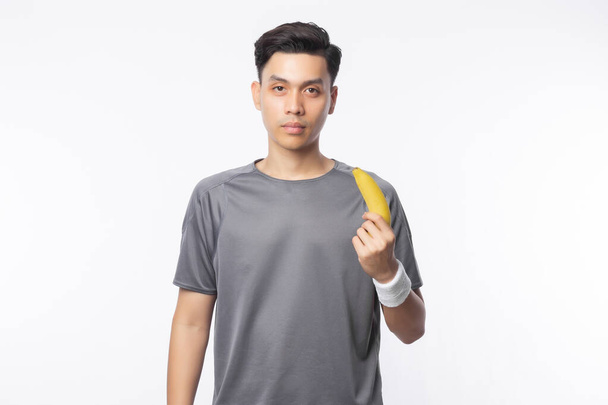 Jovem bonito asiático esporte homem segurando banana com sorrindo isolado no fundo branco. Conceito de estilo de vida saudável. - Foto, Imagem