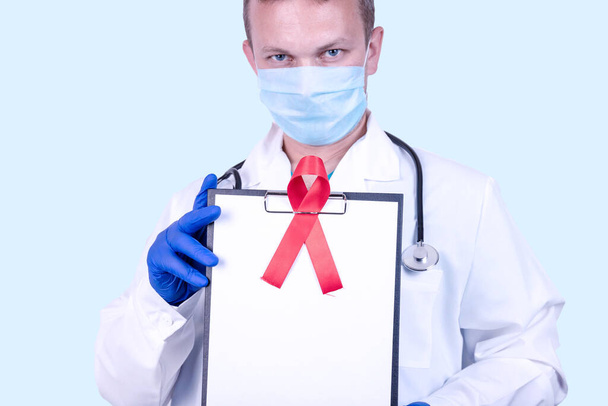 A doctor in medical gloves holds a tablet with a red ribbon - a symbol of the fight against AIDS and vasculitis and a place for text. - Fotografie, Obrázek