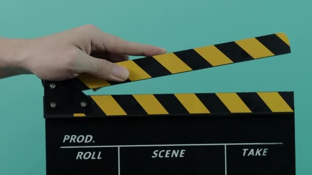 Movie slate. Close up man hand hold empty black and yellow stripe film making clapperboard isolated on blue green background studio. Clapped on and off. film slate for video production. - Footage, Video
