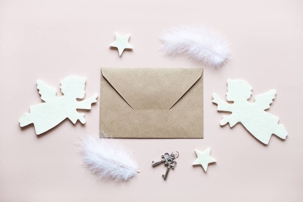 Romantic composition of craft envelope in the center, white felt angels, stars, feathers and keys on a powder pink background. Concept of love, St. Valentines day, wedding and other holidays. - Fotografie, Obrázek