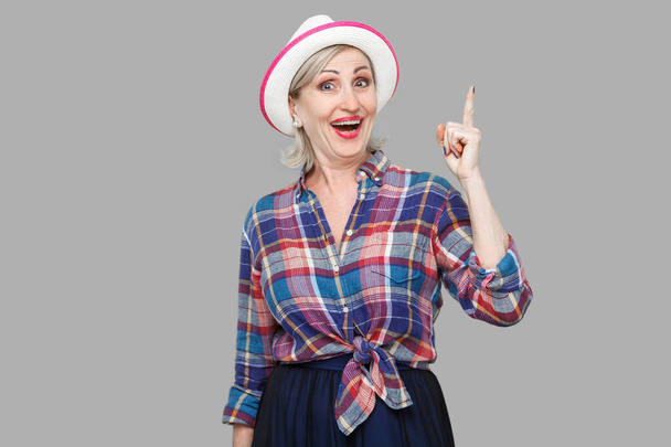 The best idea. Portrait of excited happy modern stylish mature woman in casual style with hat standing, looking at camera with good plan surprised. indoor studio shot isolated on gray background. - Photo, Image