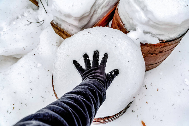 Χέρι του ανθρώπου σε φρέσκο λευκό χιόνι στην κορυφή του καφέ ξύλινο βαρέλι το χειμώνα - Φωτογραφία, εικόνα