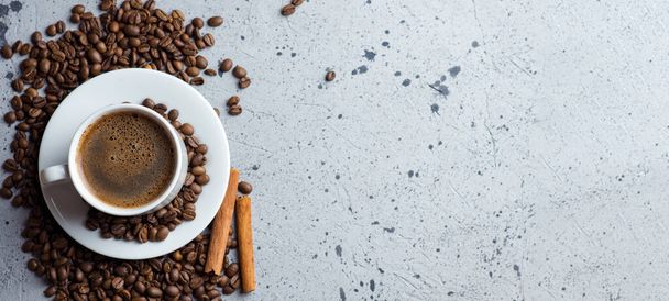 Close-up van witte espresso koffiebeker, verspreide gebrande koffiebonen en kaneel - Foto, afbeelding