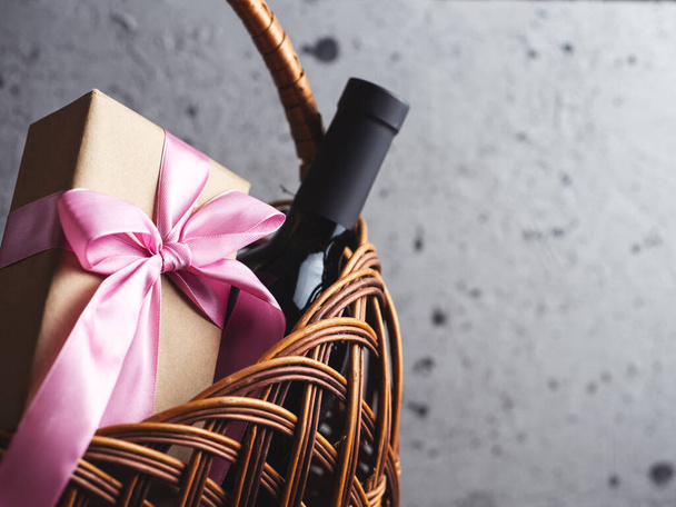 Een fles rode wijn en een geschenkdoos met een strikje in een mandje met copyspace - Foto, afbeelding