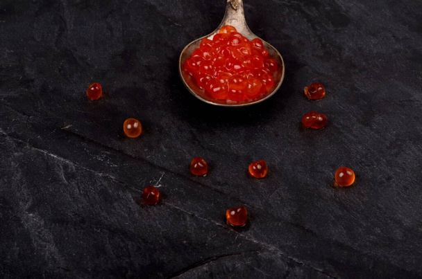 Spoon with red salmon caviar on black stone plate. Copy space.Top view. - Photo, Image