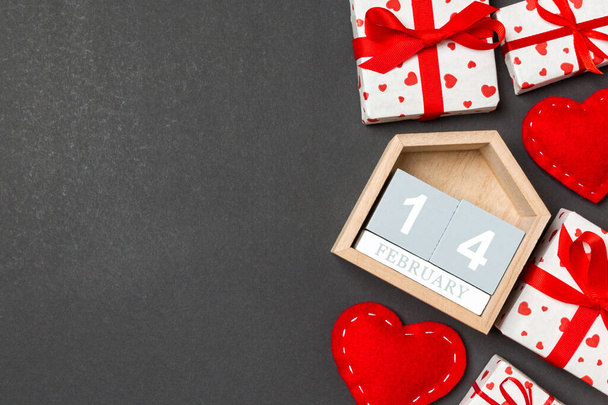 Σύνθεση διακοπών από κουτιά δώρων, ξύλινο ημερολόγιο και κόκκινες υφασμάτινες καρδιές σε πολύχρωμο φόντο με κενό χώρο για το σχεδιασμό σας. Στις 14 Φεβρουαρίου. Κάτοψη της έννοιας Ημέρα του Αγίου Βαλεντίνου. - Φωτογραφία, εικόνα