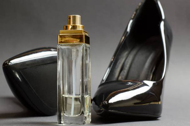 Perfume de mujer y un par de zapatos de charol negro sobre fondo negro. - Foto, imagen