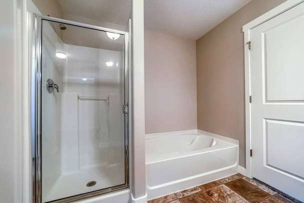 Suihkukaappi ja kylpyamme puhtaan kylpyhuoneen sisällä, jossa on ruskeat laatat lattialla - Valokuva, kuva