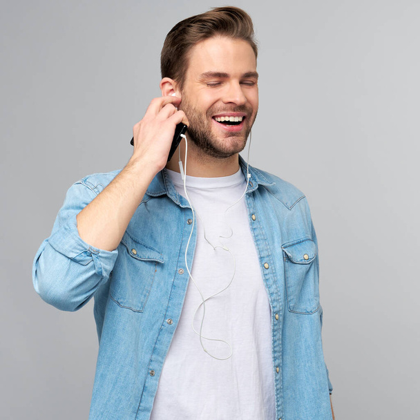 Close up portrait of cheerful young man enjoying listening to music wearing casual jeans outfit - Foto, Imagen