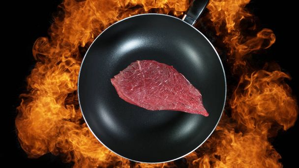 Beef steak in pan, flames on background. High angle view of meat preparation, studio shot. - Fotografie, Obrázek