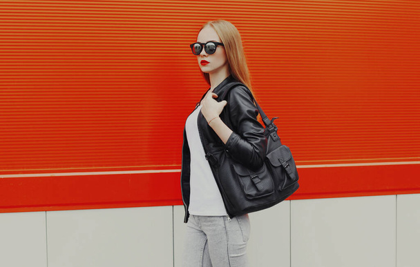 Stylish woman with bag walking in the city on a red background - Foto, imagen