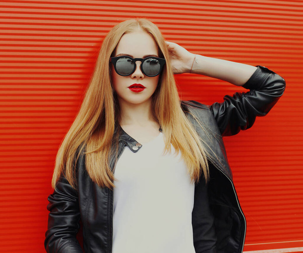 Portrait of young blonde woman in sunglasses on a red background - 写真・画像