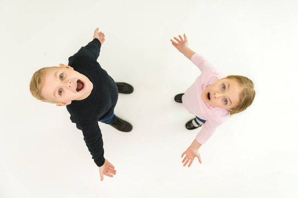 Los dos niños sorprendidos se paran sobre el fondo blanco. Vista desde arriba - Foto, imagen