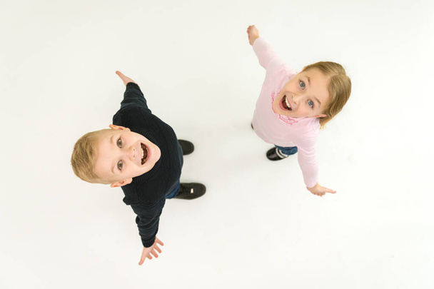 Los dos niños ríen parados sobre el fondo blanco. Vista desde arriba - Foto, imagen