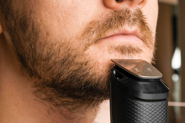 Adam kısa sakalını tıraş ediyor. Elektrikli tıraş makinesinden sonra sinirlilik.  - Fotoğraf, Görsel