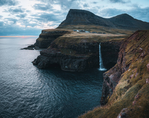 Gasadalur village and Mulafossur its iconic waterfall during sunset in summer with bluw sky. Vagar, Faroe Islands, Denmark. Rough see in the north atlantic ocean. - Zdjęcie, obraz