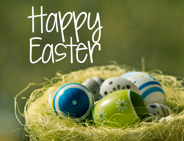 Huevos de Pascua en canasta wisker en la naturaleza con texto Feliz Pascua
 - Foto, Imagen