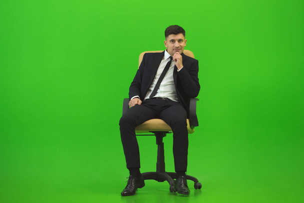 Человек сидит на стуле на зеленом фоне - Фото, изображение