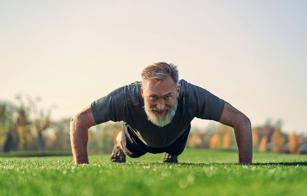 Stary sportowiec pchający się na trawę - Zdjęcie, obraz