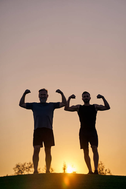 Les deux sportifs montrant des muscles sur le fond du coucher du soleil - Photo, image