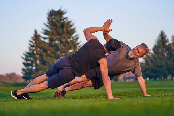 The young and old sportsmen push up together on the grass - Photo, Image