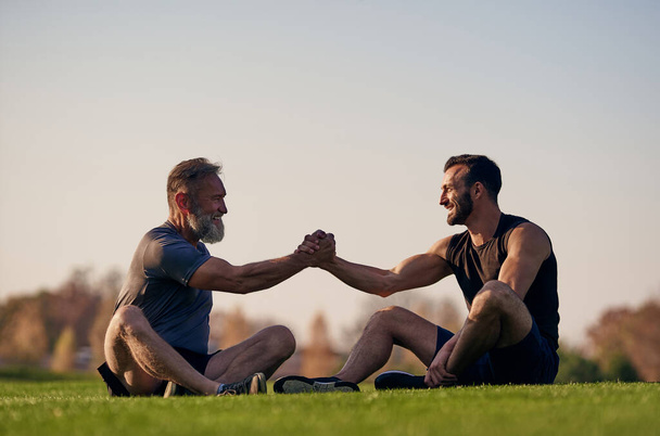 Двое счастливых мужчин сидят на траве и приветствуют - Фото, изображение