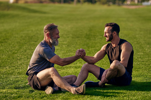 Dva šťastní muži sedící na trávě a zdravící - Fotografie, Obrázek