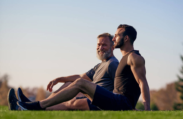 The old and young sportsmen sitting on the grass - Photo, Image