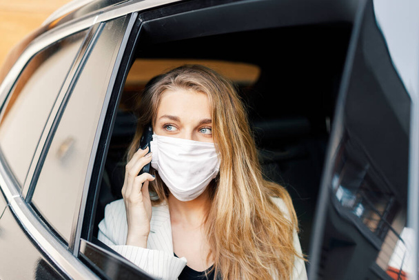 Молодая бизнесвумен в защитной маске разговаривает по телефону и водит машину во время пандемии  - Фото, изображение