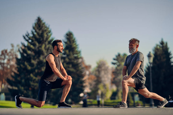 De jonge en oude atleten stretching outdoor - Foto, afbeelding