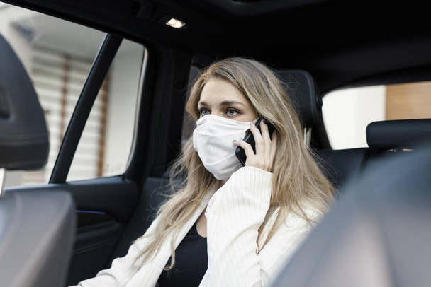 Młoda bizneswoman w masce ochronnej rozmawia przez telefon i prowadzi samochód w czasie pandemii  - Zdjęcie, obraz