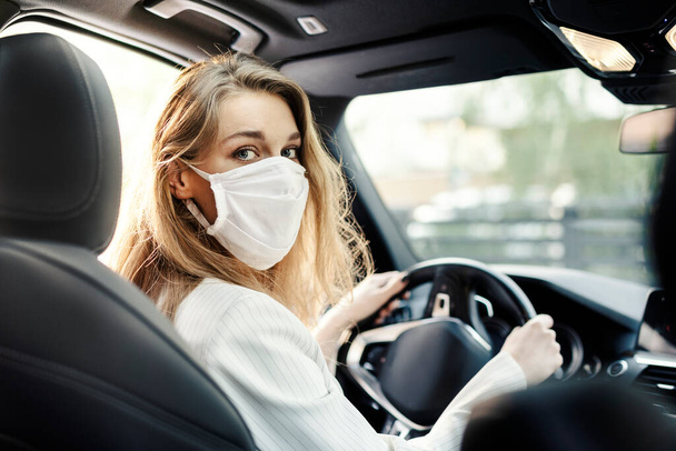 Una giovane donna d'affari con una maschera protettiva sta guidando un'auto in una pandemia  - Foto, immagini