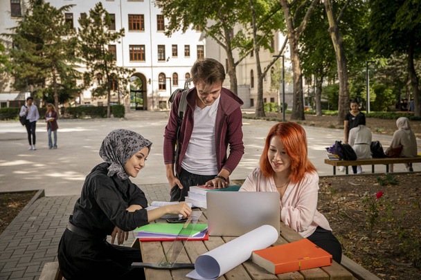 Mladí studenti studují společně, chatují, dívají se na počítač, sledují filmy a smějí se v zahradě školy. Univerzita, areál, školní zahrada, muslimský student, křesťan, Žid, různí lidé - Fotografie, Obrázek