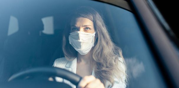 Nuori liikenainen suojelevassa naamiossa ajaa autoa pandemiassa.  - Valokuva, kuva