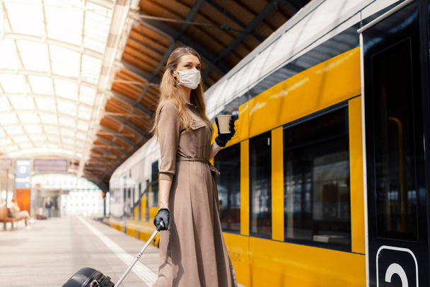 Mladá žena se zavazadly má na sobě bezpečnostní masku, zatímco používá veřejnou dopravu - Fotografie, Obrázek