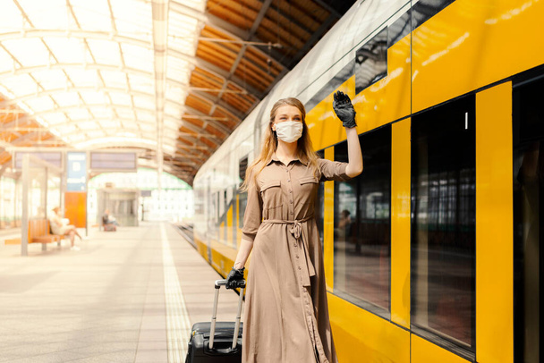 Eine junge Frau mit Gepäck trägt eine Schutzmaske, während sie die öffentlichen Verkehrsmittel benutzt - Foto, Bild